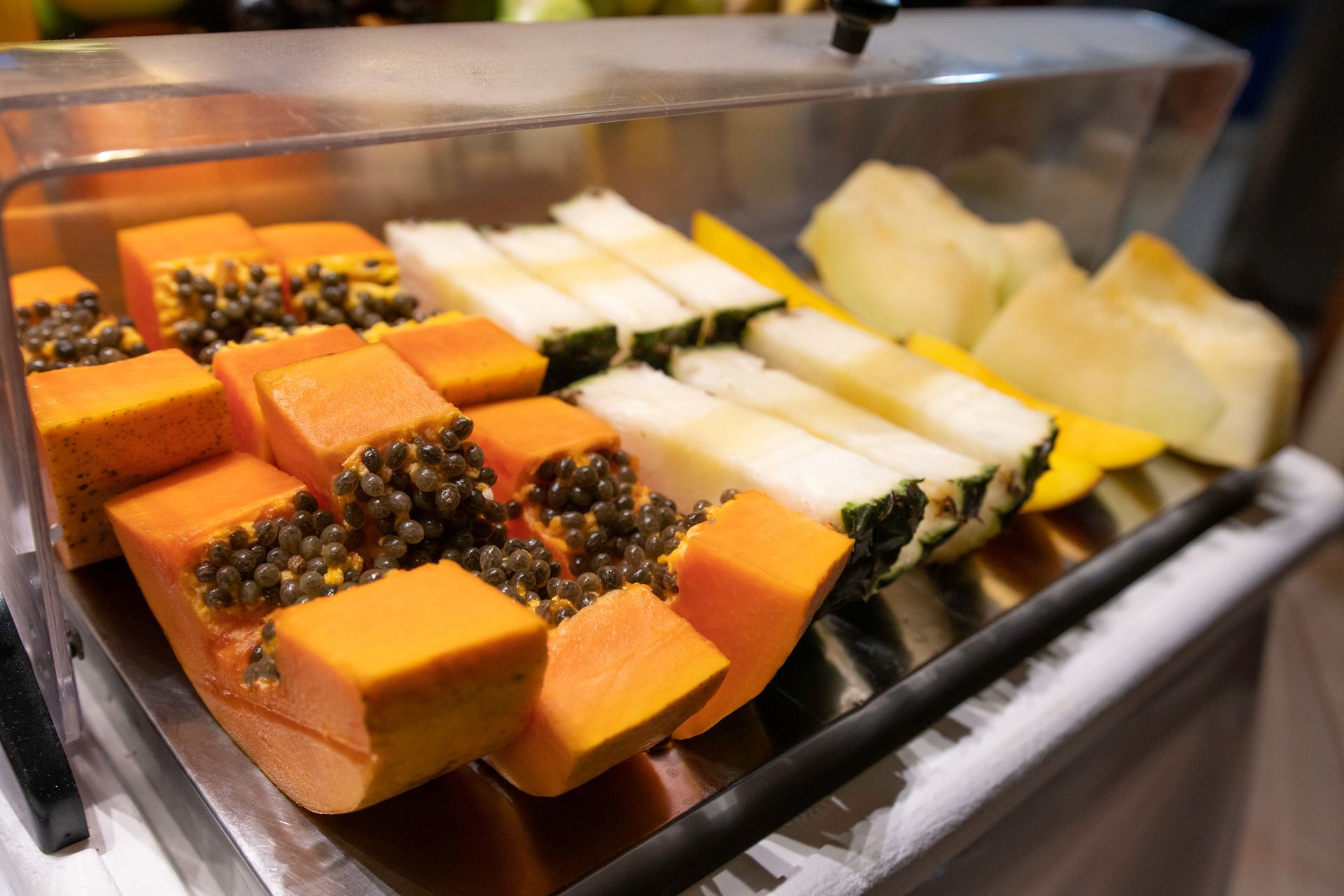 Uma bandeja de frutas fatiadas, incluindo mamão e abacaxi, sobre uma mesa.