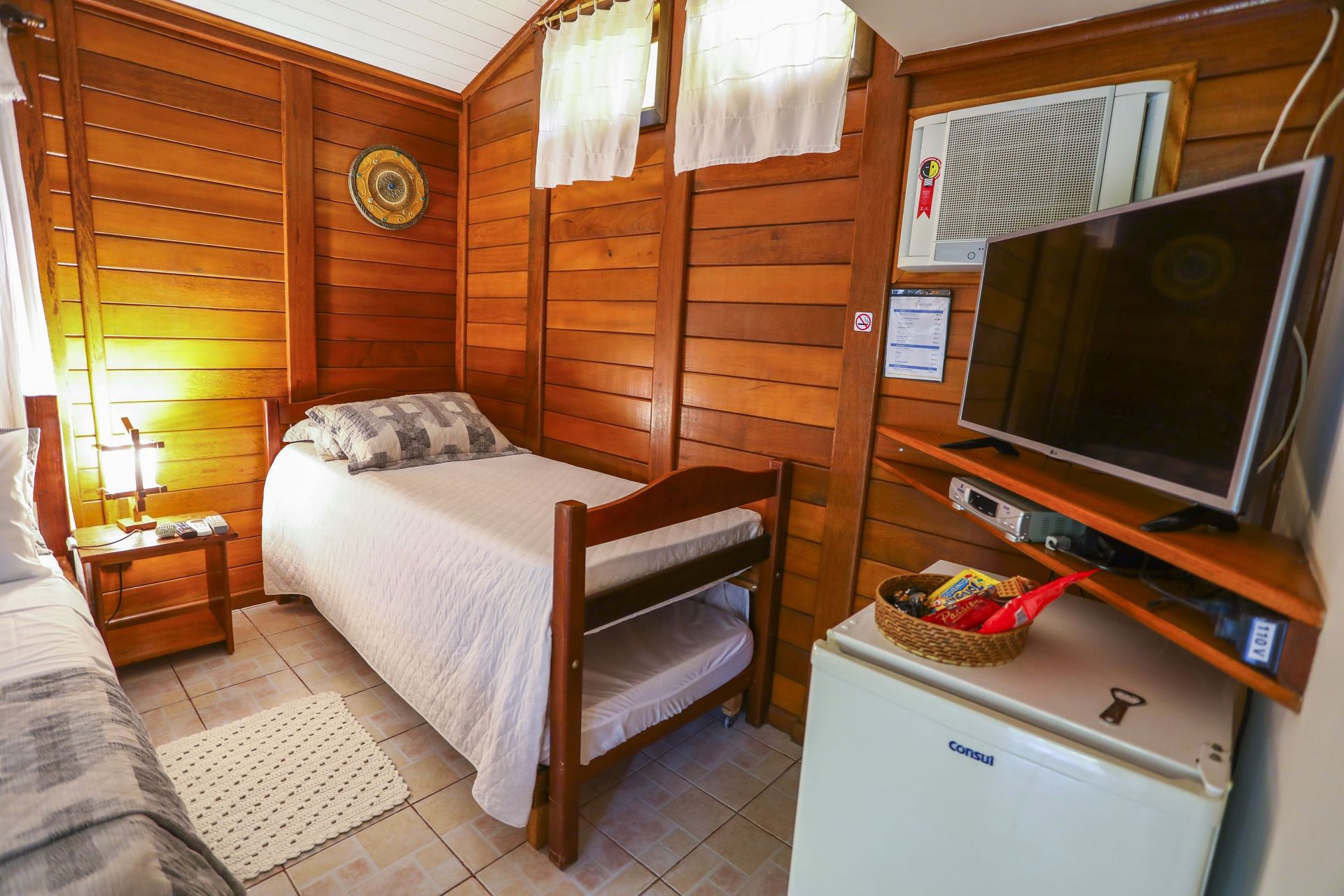 Um quarto com cama, televisão, geladeira e ar condicionado.