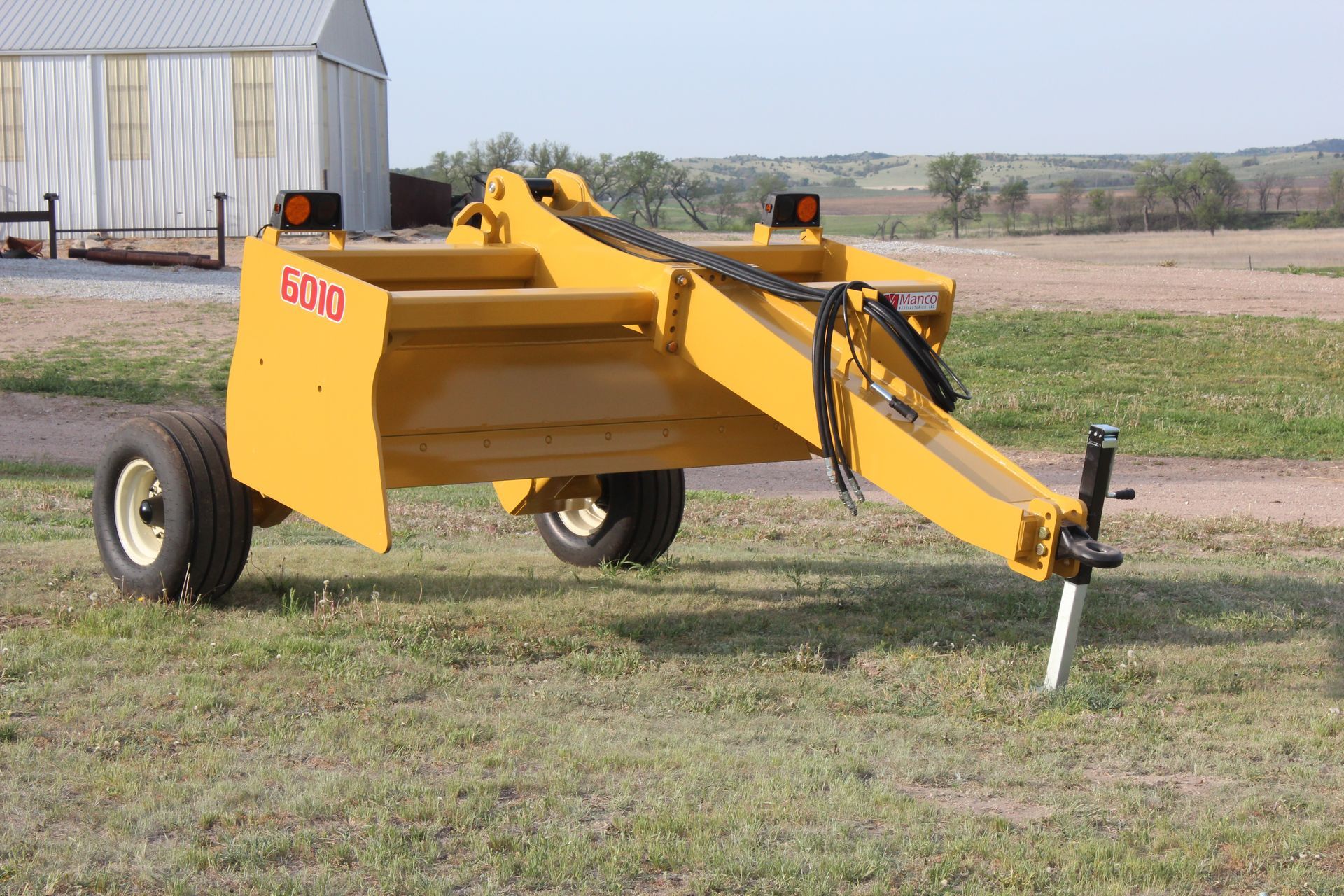 A yellow scraper is parked in a grassy field.