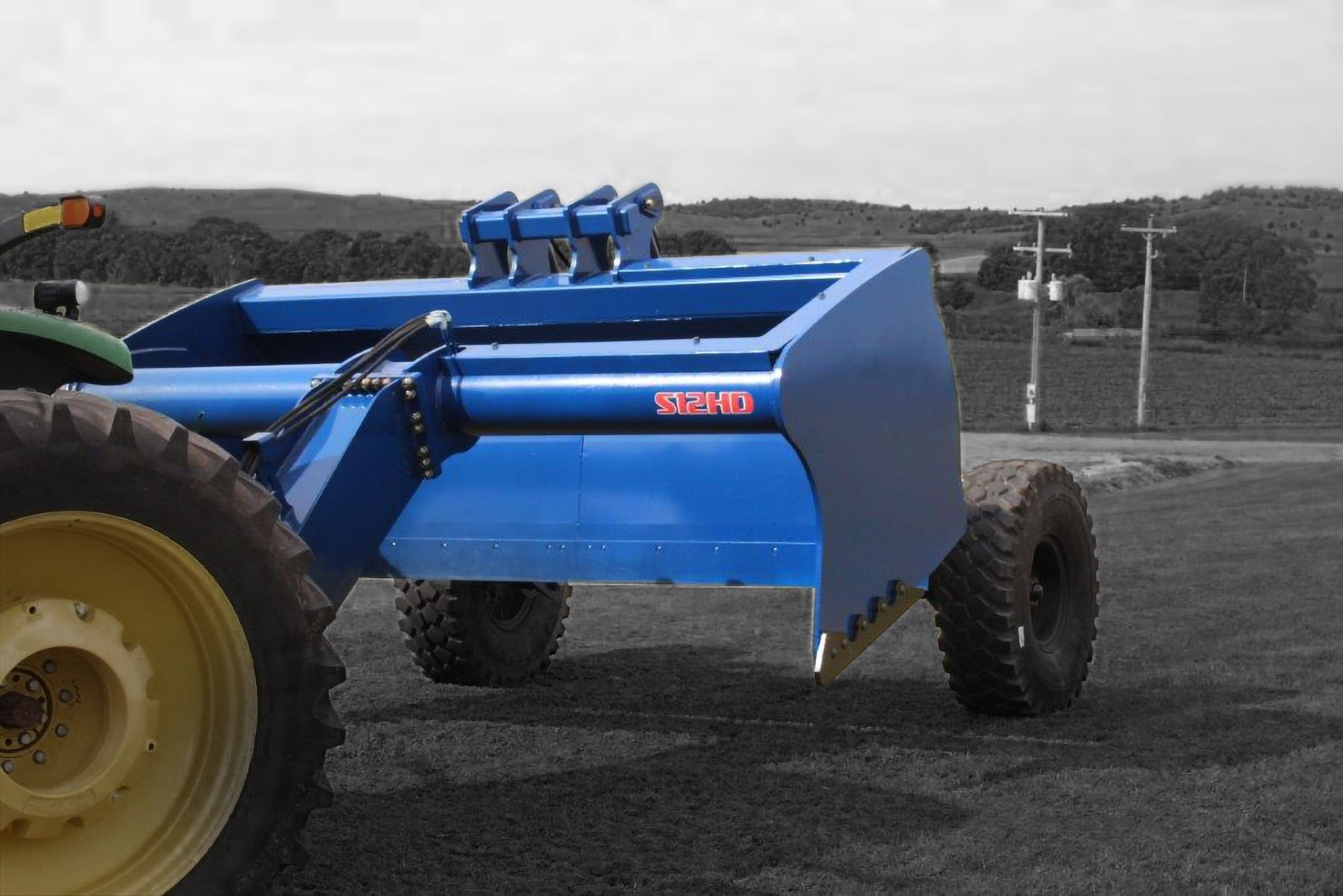A blue scraper is parked next to a yellow tractor