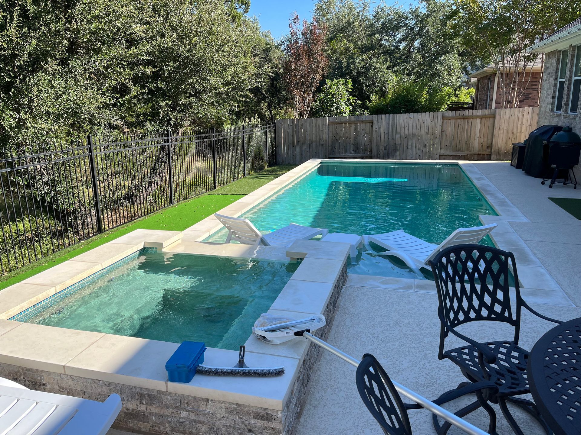 Backyard pool with a shallow hot tub, turquoise water, lounge chairs, and a fence-lined yard