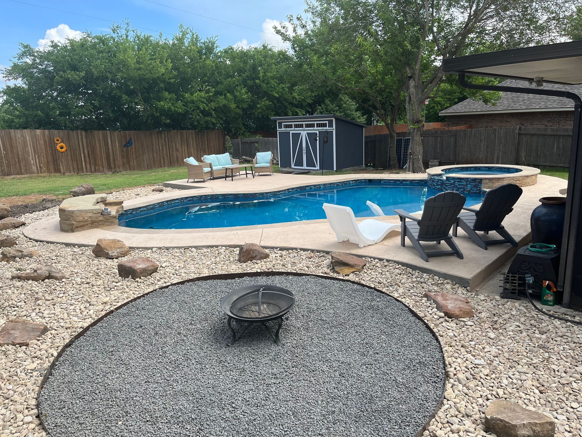 Backyard pool with patio chairs and a gravel fire pit under a cloudy sky