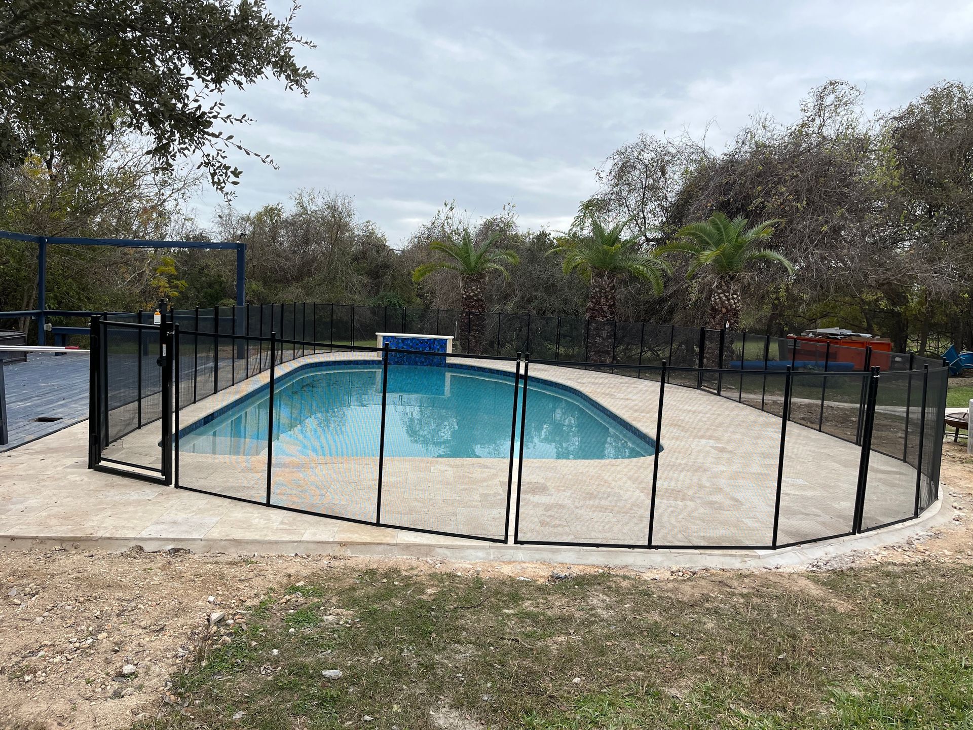 Outdoor swimming pool enclosed by a black fence, with trees and cloudy sky in the background.