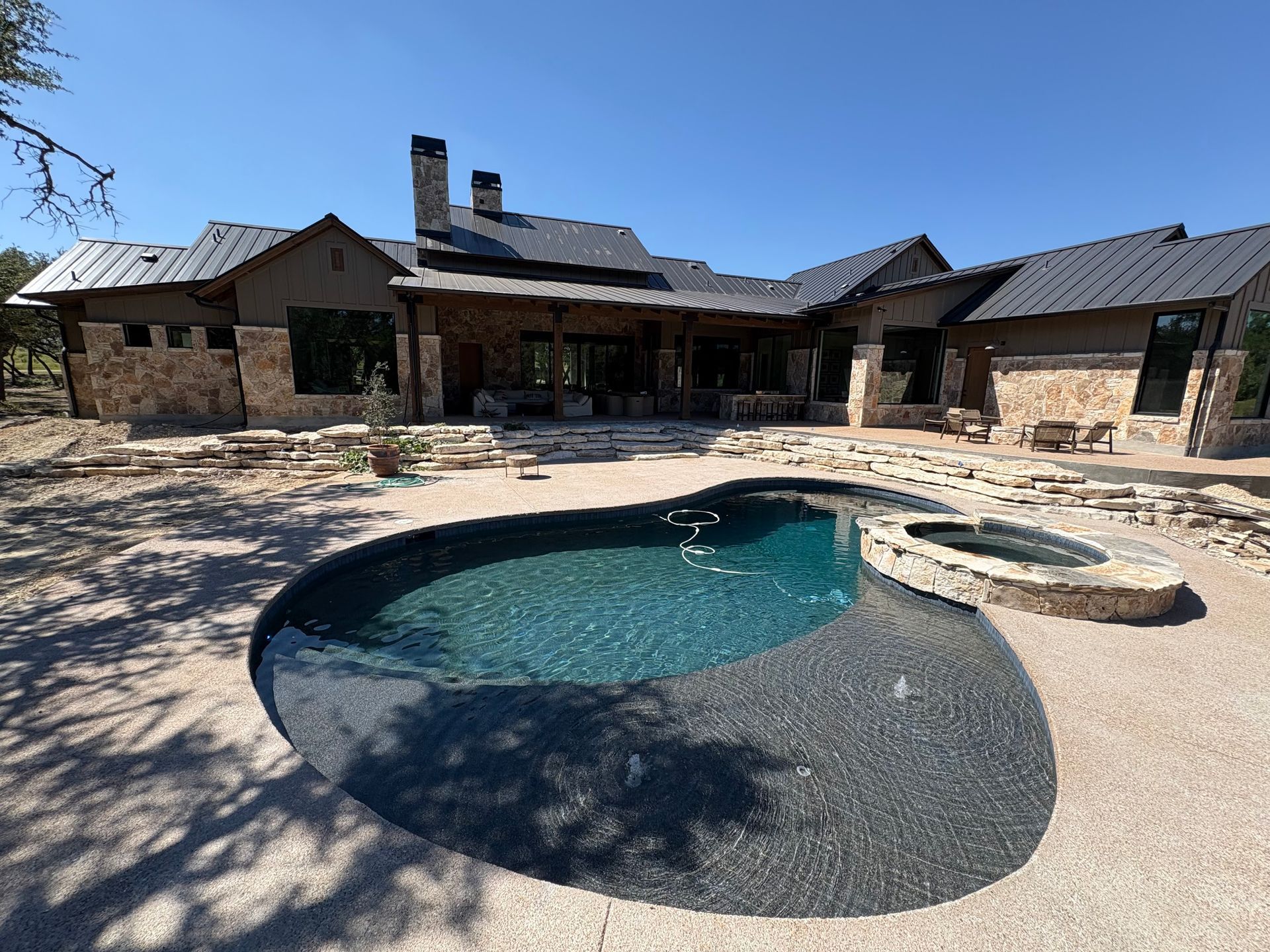 Stone house courtyard with a pool and hot tub in bright sunlight