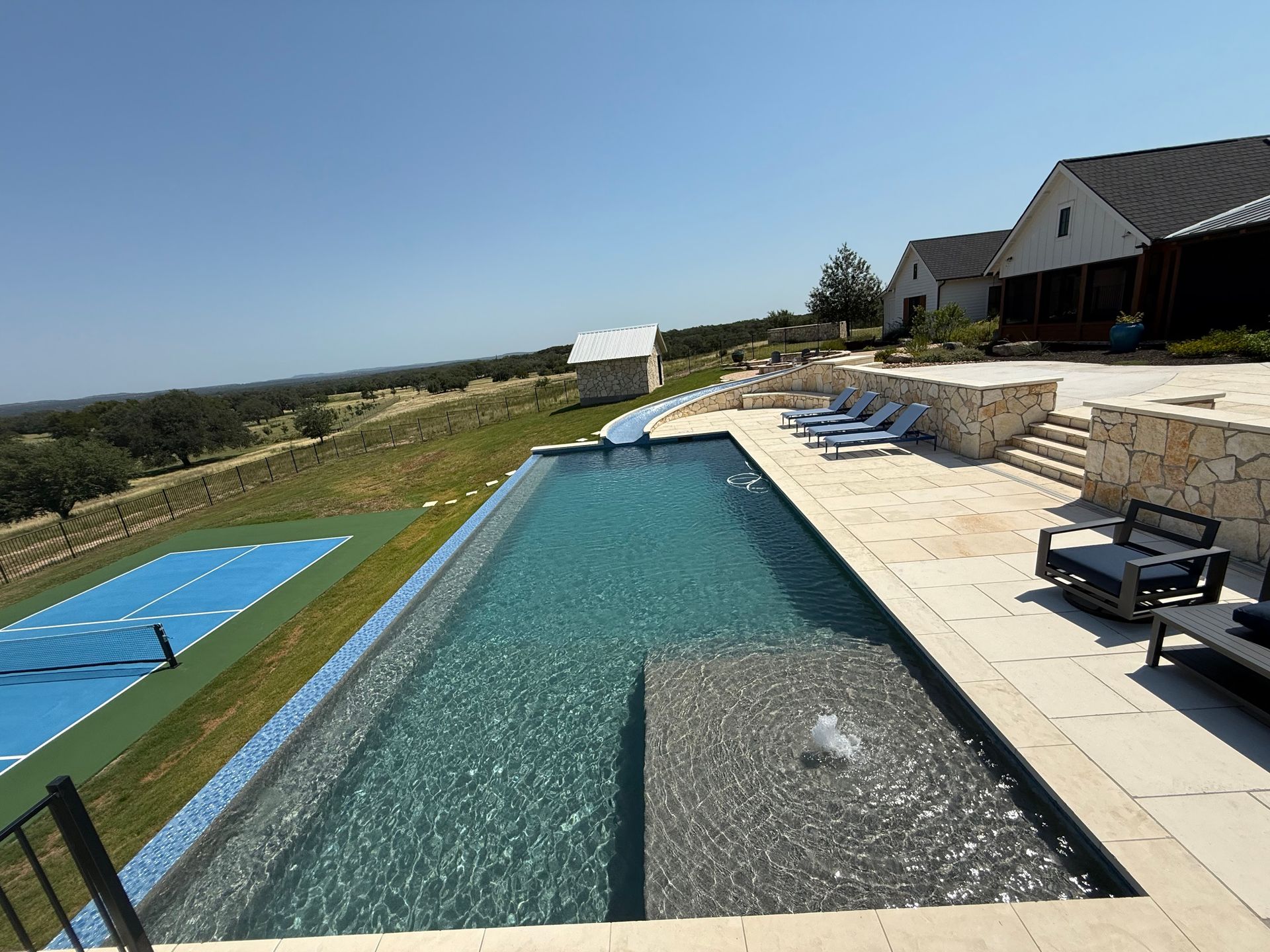 Outdoor infinity pool overlooking a hillside, with lounge chairs and a blue sky on a sunny day