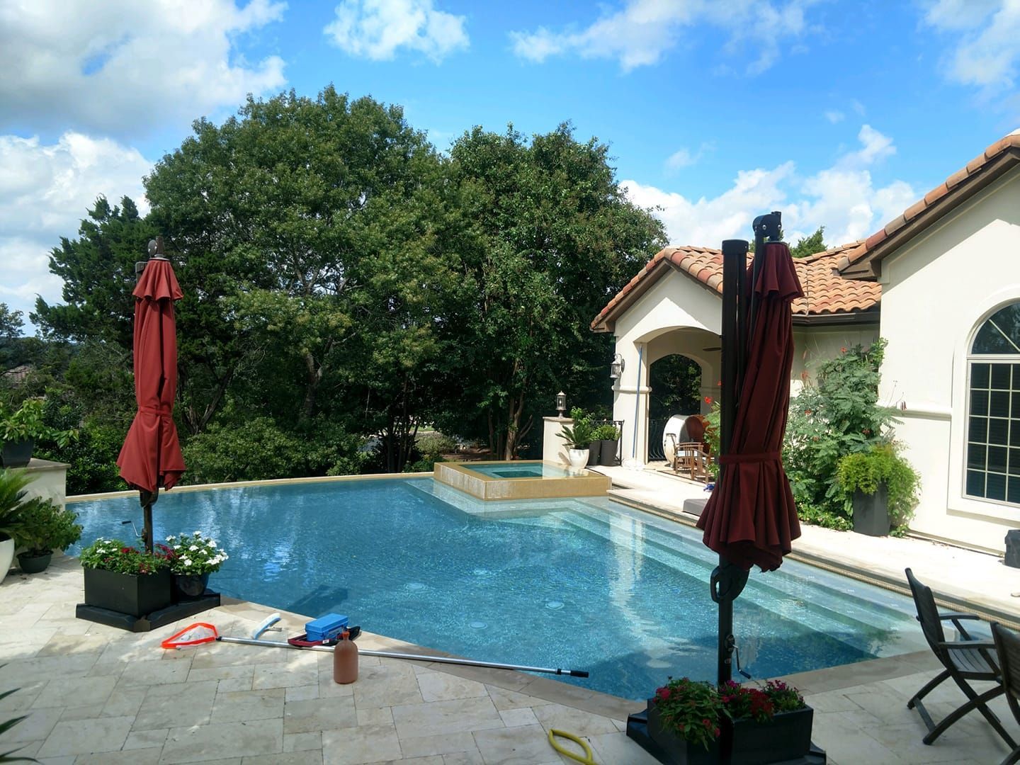Backyard pool with closed red umbrellas, lounge chairs, and a house under a blue sky