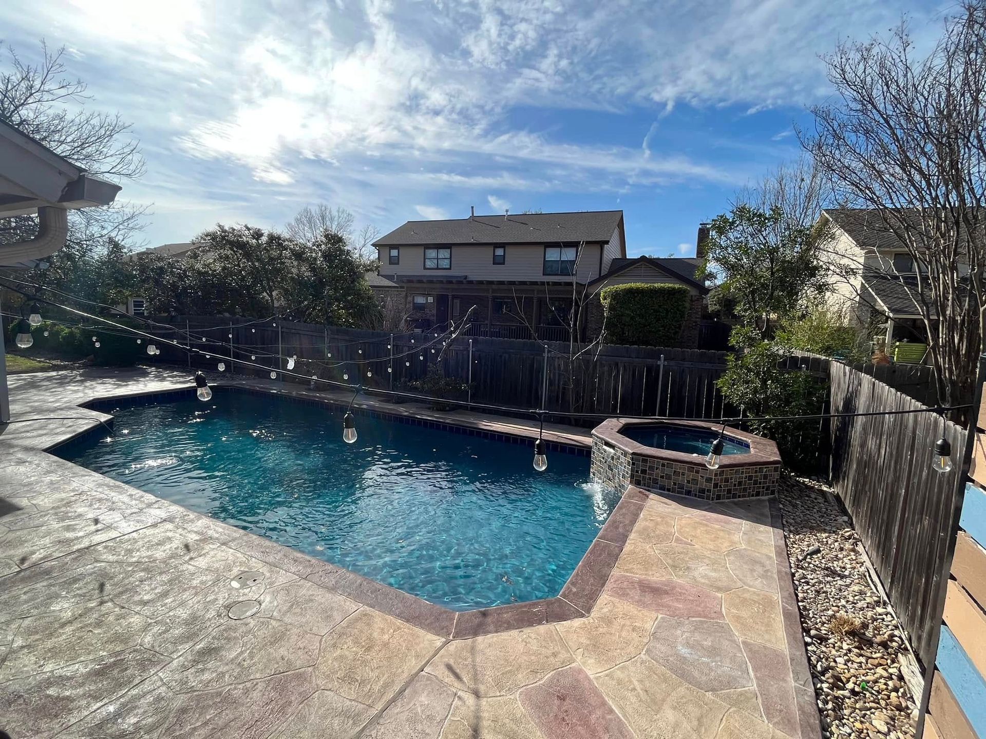 Backyard swimming pool with patio, hot tub, fence, and sunny sky