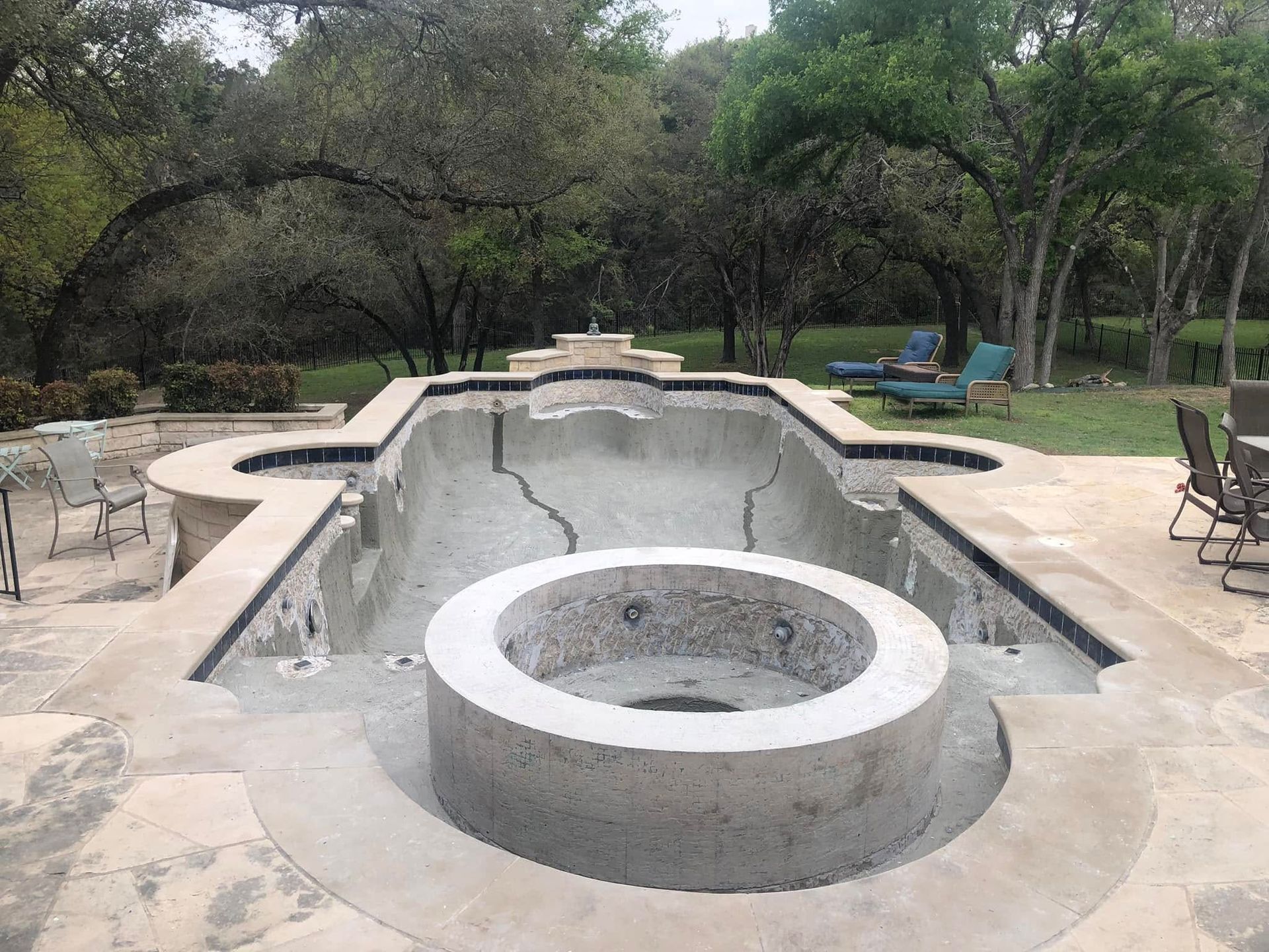 Empty backyard swimming pool with a circular hot tub in the foreground and patio furniture around it