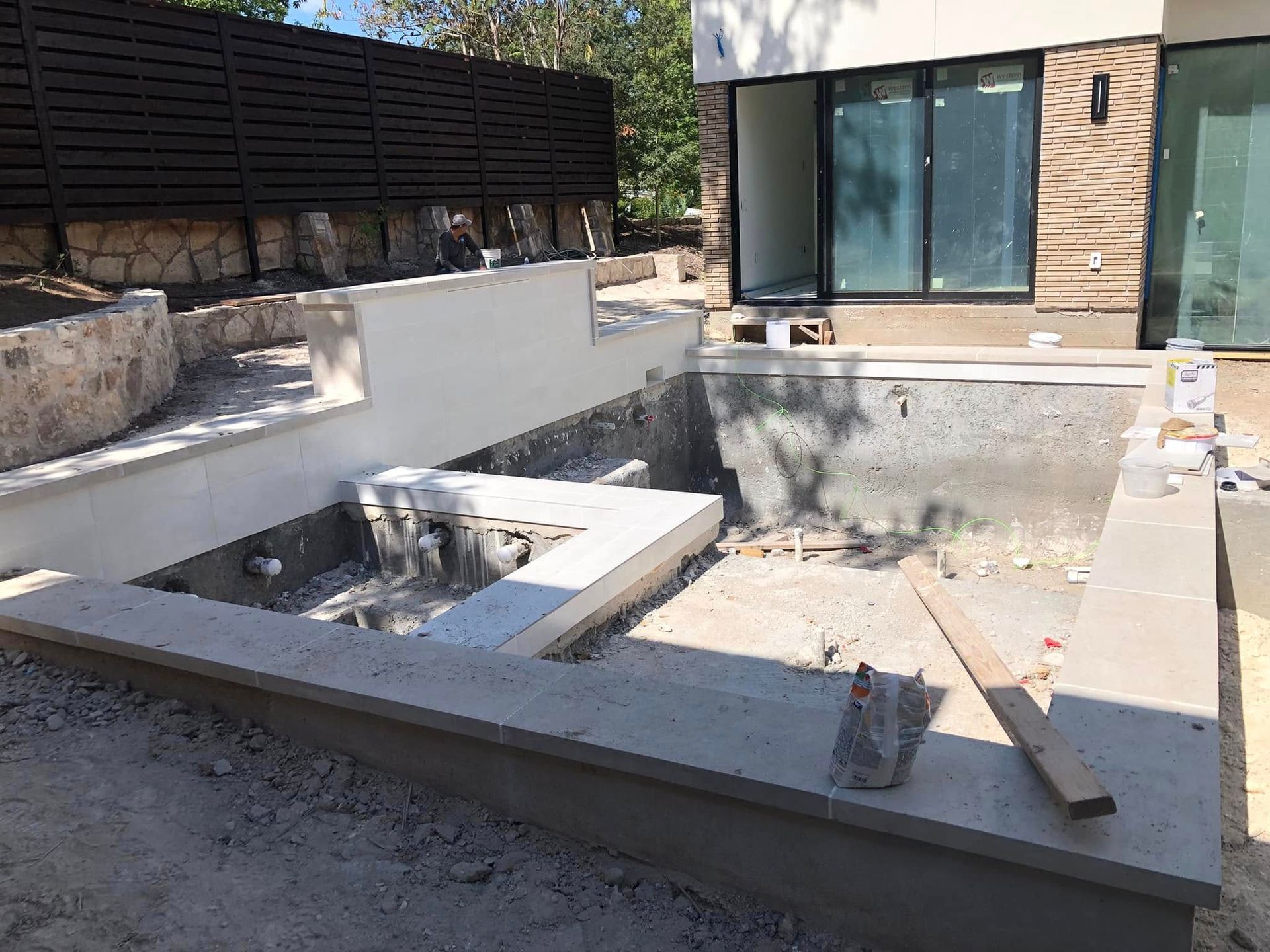 Modern backyard patio with a sunken concrete fire pit and built-in seating near a glass-walled house