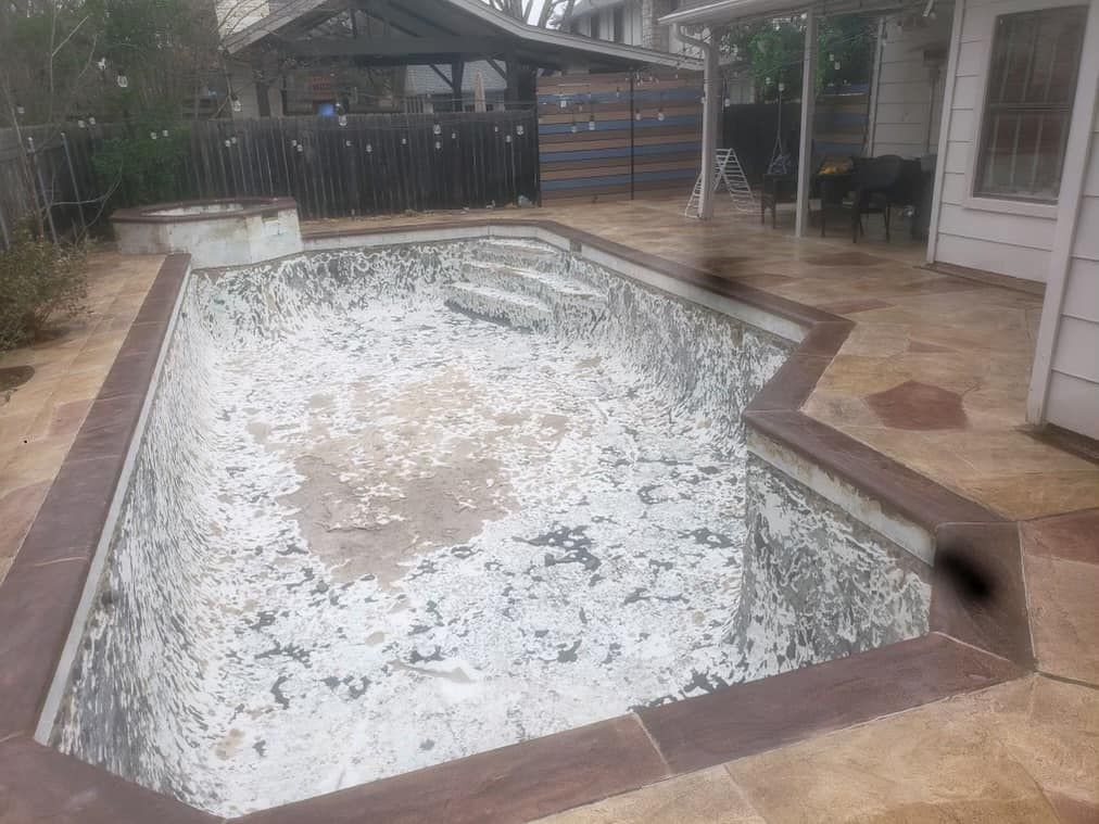 Empty drained swimming pool beside a patio, with brown coping and a tiled surface showing debris and stains