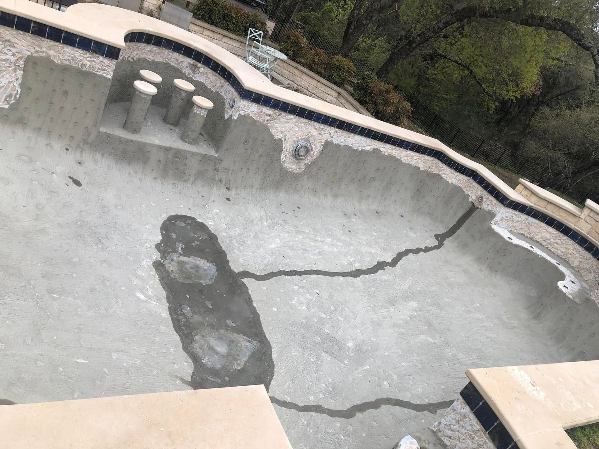 Empty drained pool with cracked concrete and dark stains, viewed from above.