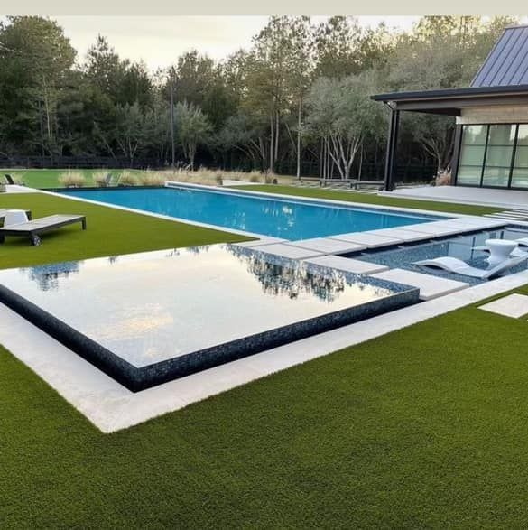 Modern backyard with long pool, reflecting pond, lounge chair, and house beside green lawn