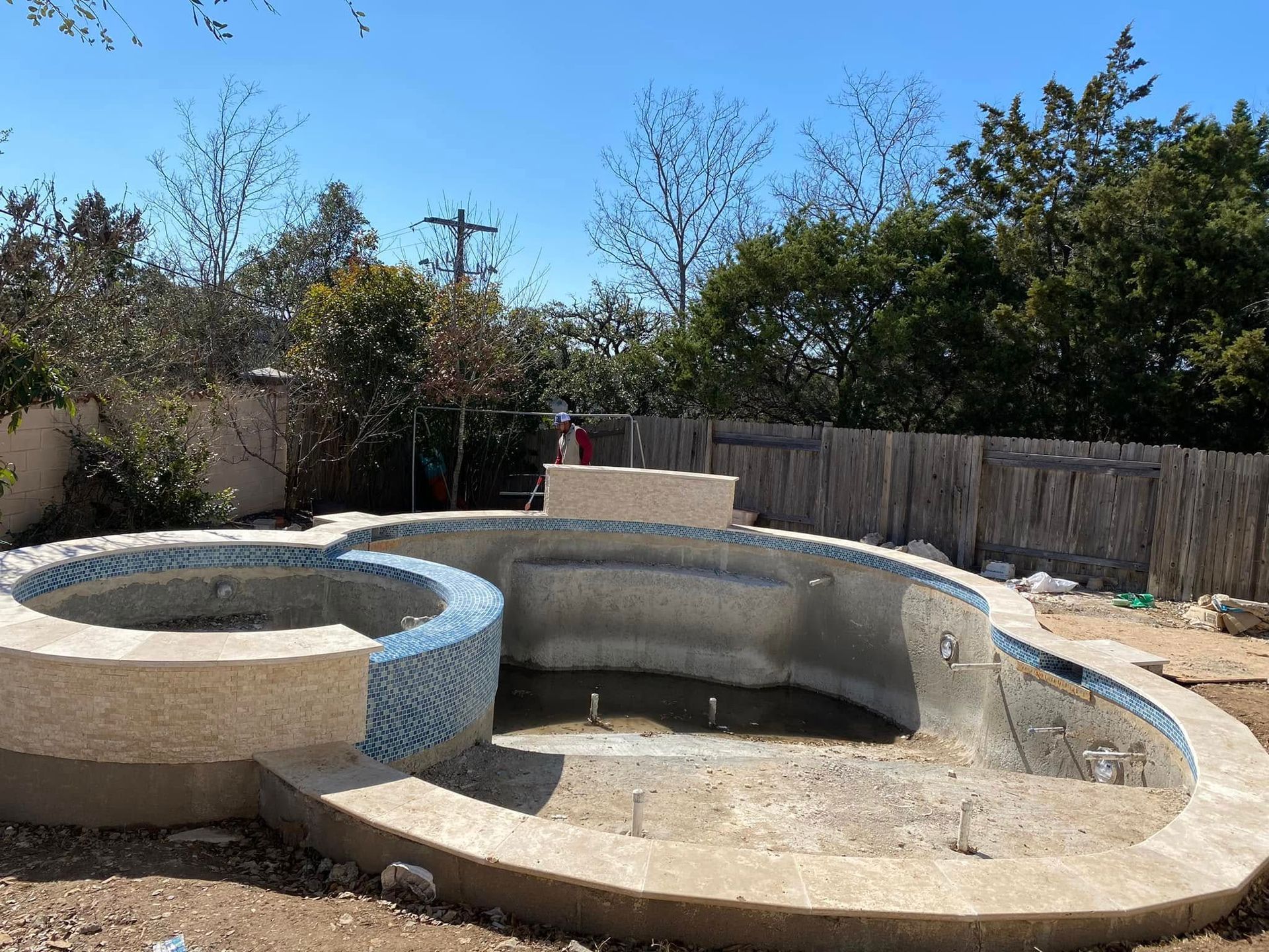 Empty backyard pool and spa under construction with concrete walls and blue sky