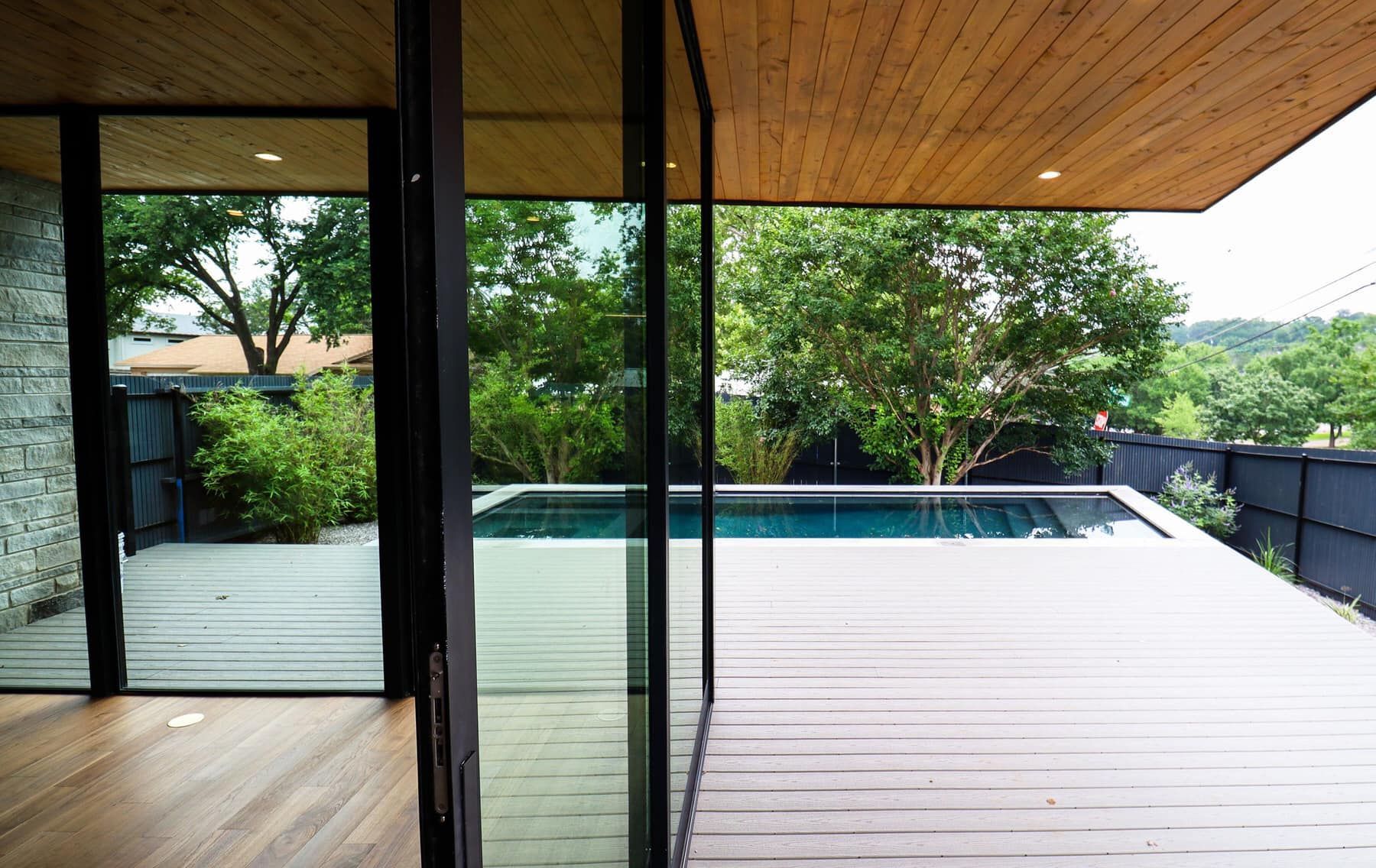 Modern patio with wood ceiling, glass wall, and pool deck overlooking green trees