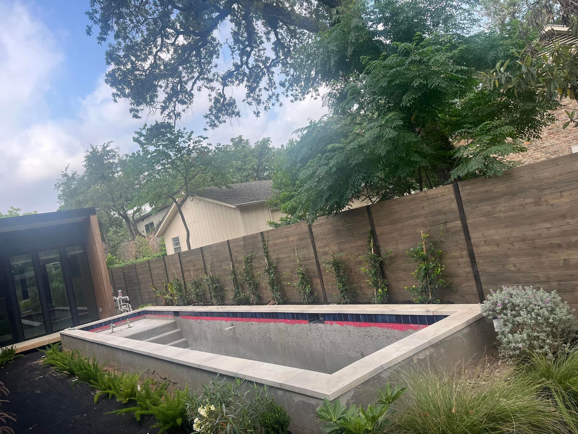Modern backyard with a rectangular pool, wooden fence, and trees overhead