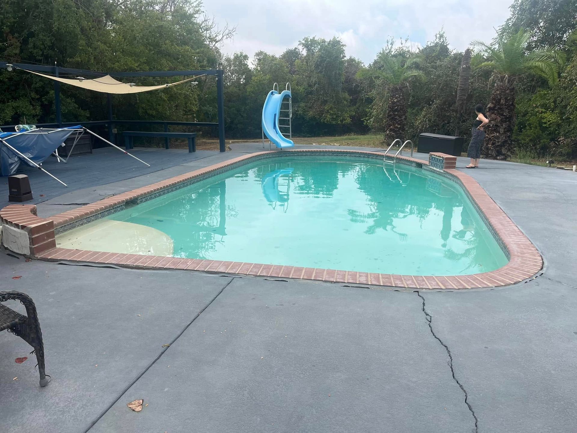 Backyard pool with turquoise water, blue slide, lounge chairs, and surrounding trees