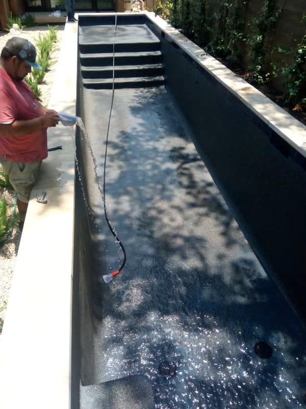 Worker lining a long rectangular pool with black waterproof material outdoors