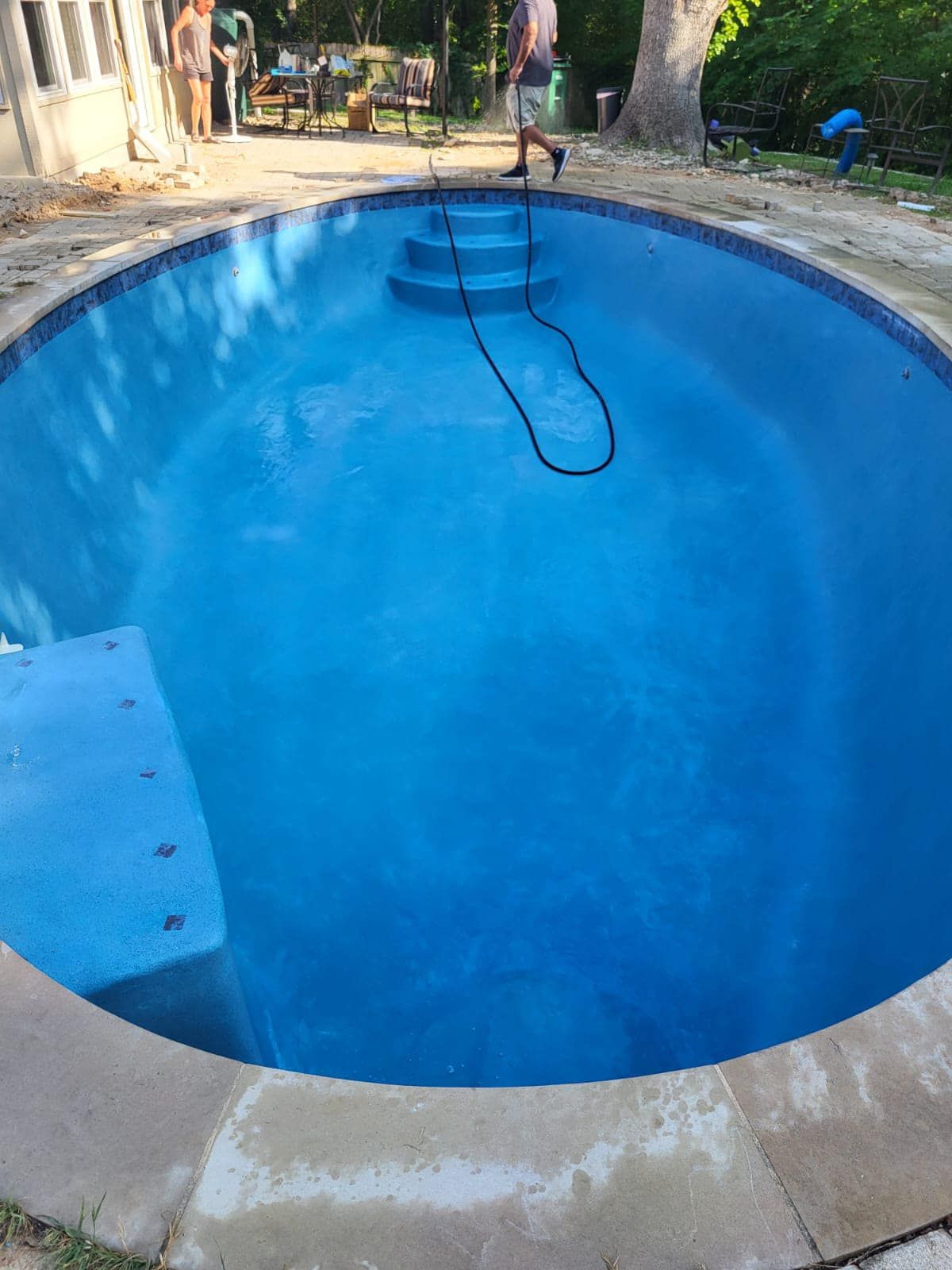 Empty blue swimming pool with a hose draped across the water and yard visible around it