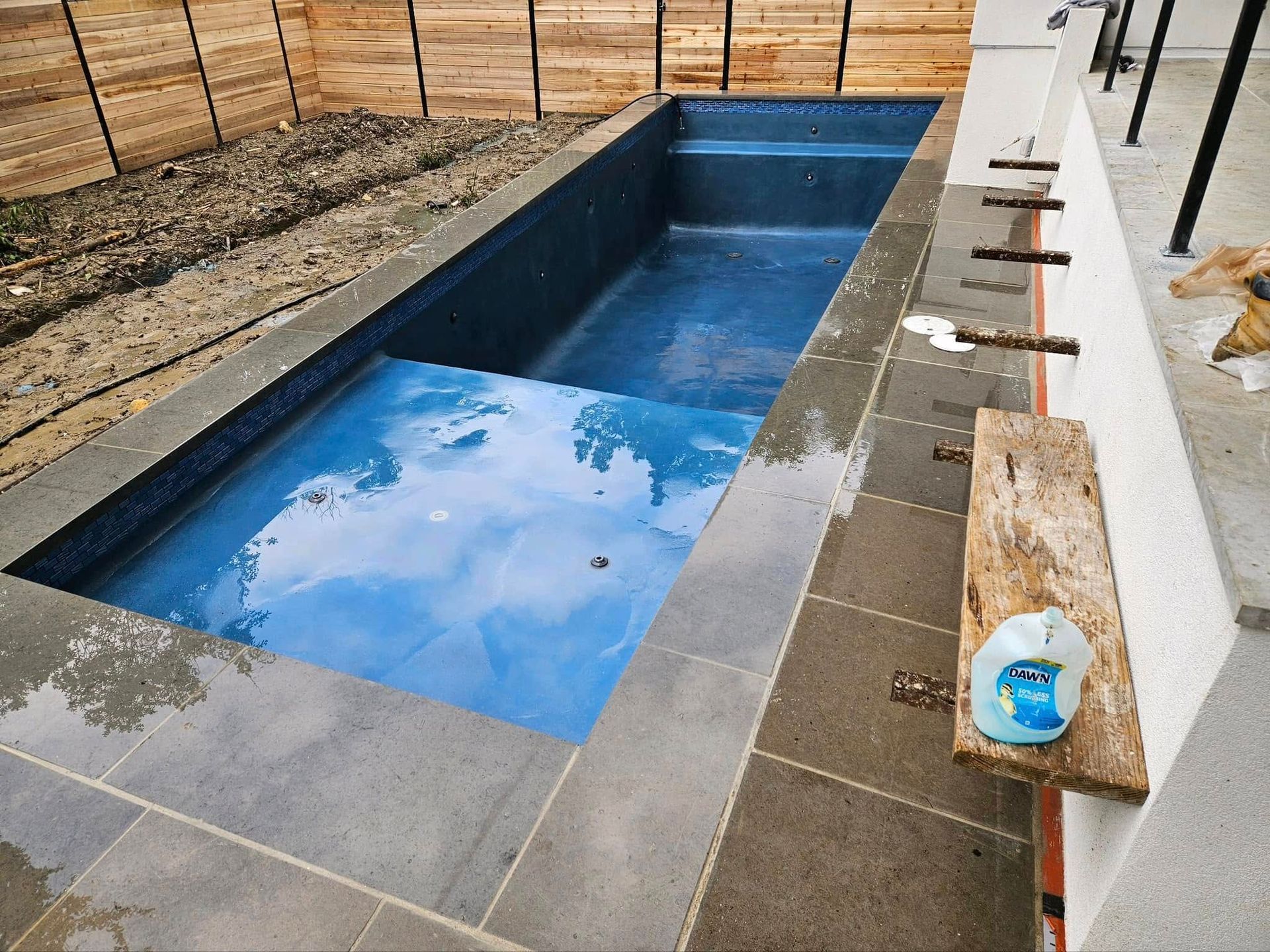 Rectangular backyard pool under construction, with blue water and unfinished surrounding deck.