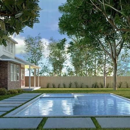 Modern backyard pool beside a house, with stone pavers, trees, and a high fence under a blue sky