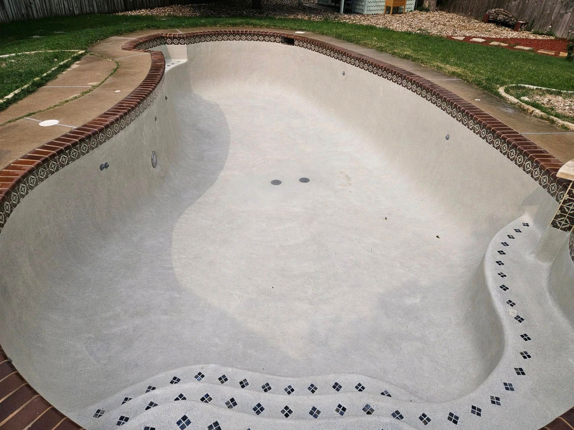 Empty swimming pool with white interior, brick coping, and gravel landscaping around the edges