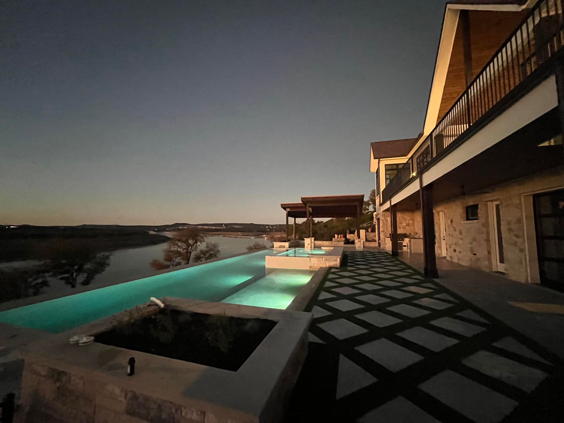 Luxury resort patio with infinity pool at sunset, overlooking a river or lake