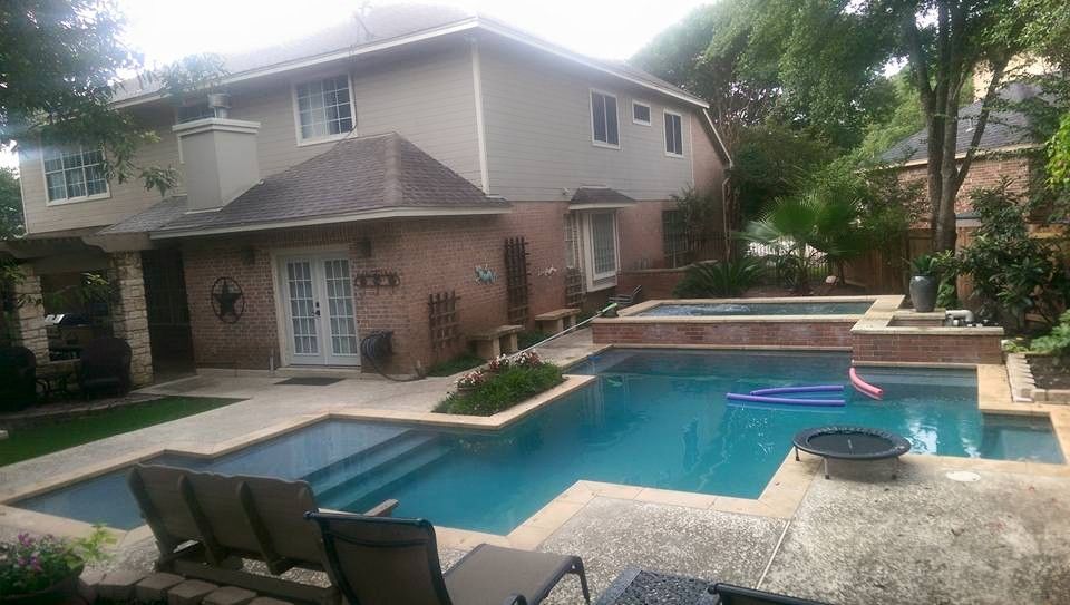 Backyard with a blue swimming pool, patio chairs, and a two-story house surrounded by trees