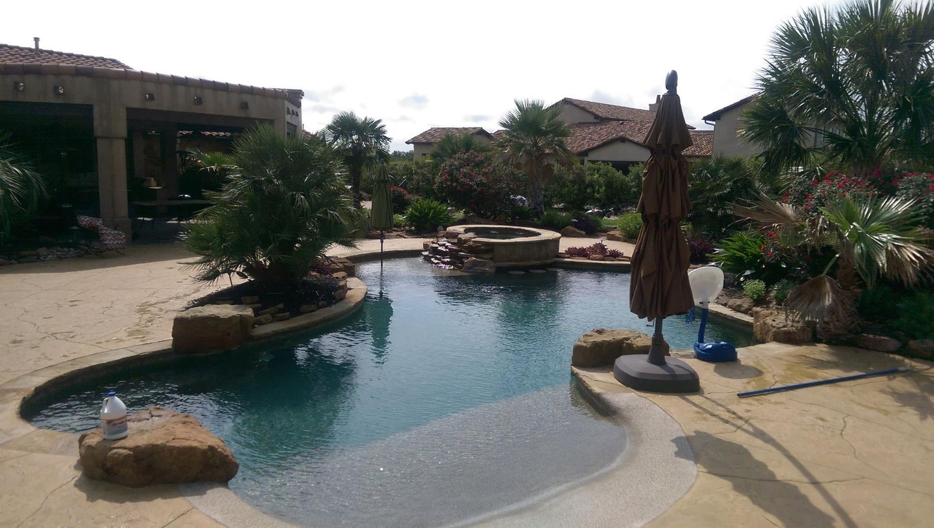 Resort pool with a small island, blue water, lounge chairs, and palm trees under a bright sky