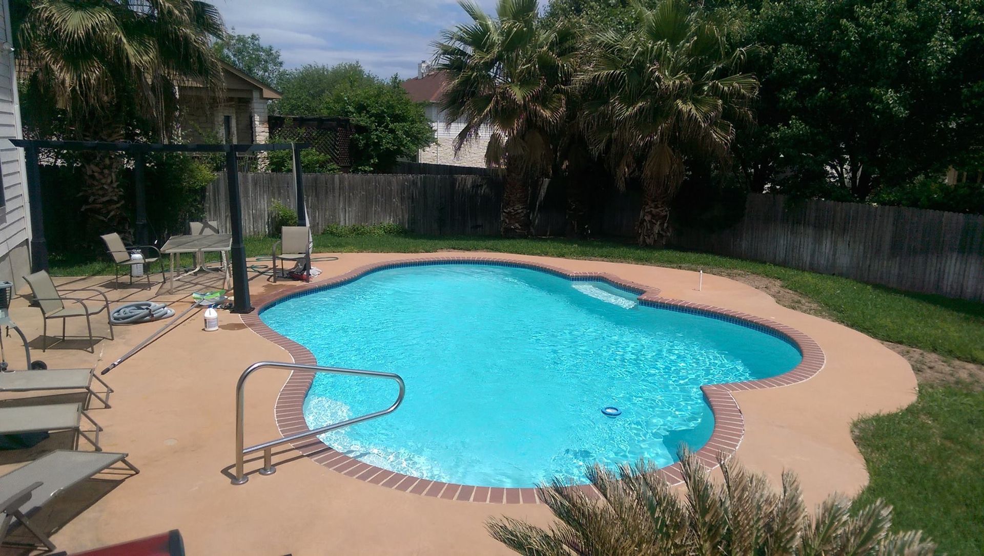 Backyard swimming pool with blue water, patio chairs, and a garden hose on the deck