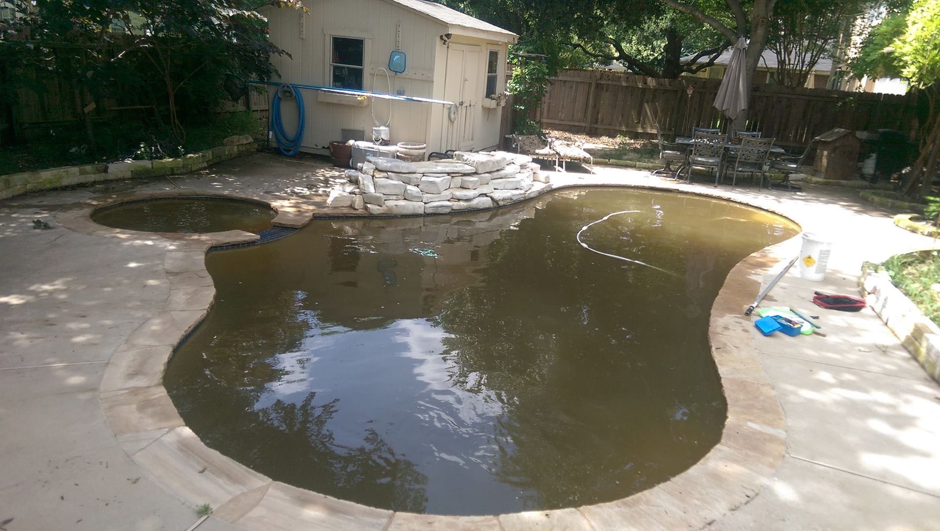 Backyard patio with a large dark puddle of standing water near a small shed and trees