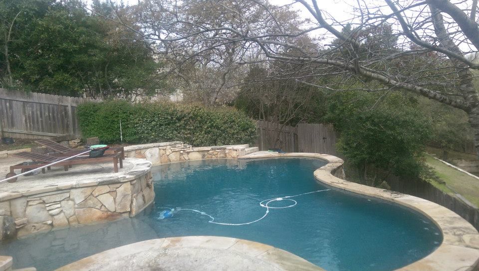 Backyard swimming pool with stone patio, wooden fence, and trees around it