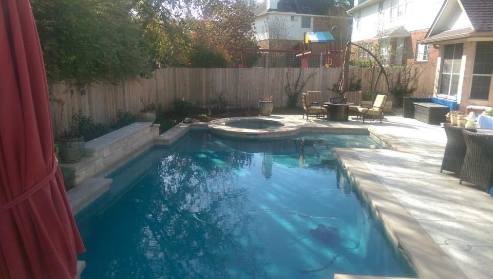 Backyard swimming pool with blue water, patio chairs, wooden fence, and a covered grill area