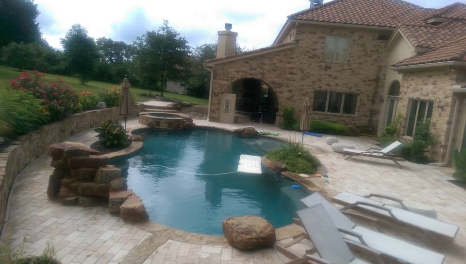 Backyard pool with stone patio, lounge chairs, and a stone house beside the water
