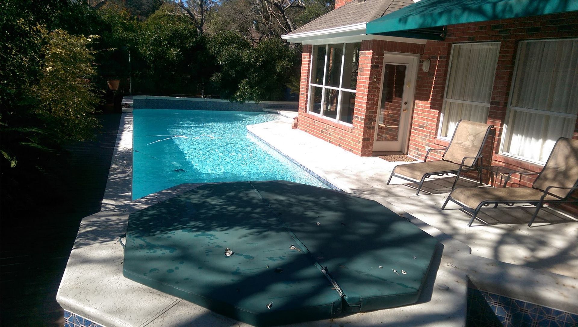 Backyard swimming pool beside a brick house with patio chairs and a covered hot tub.