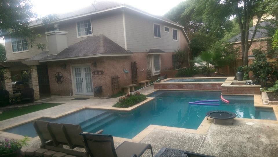 Backyard swimming pool with hot tub, patio chairs, and a two-story house in the background