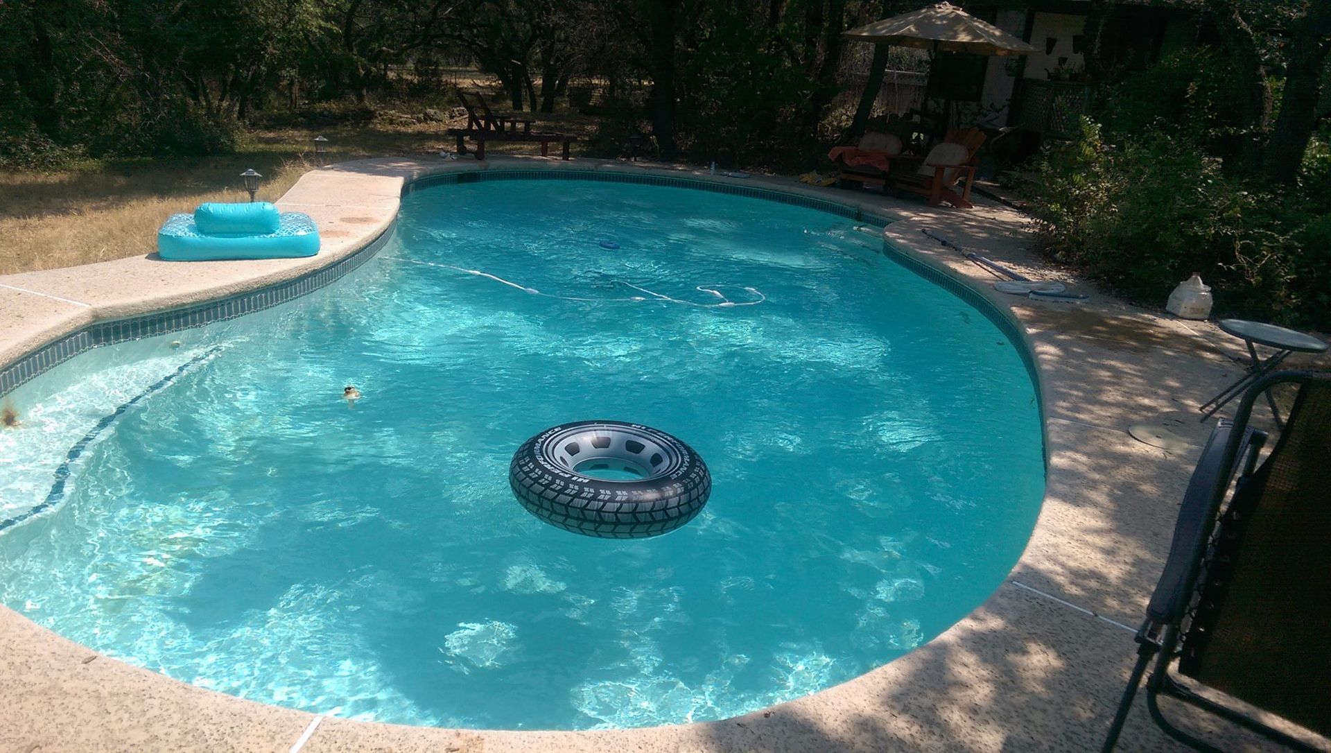Backyard swimming pool with a floating inner tube and a blue pool float on the deck