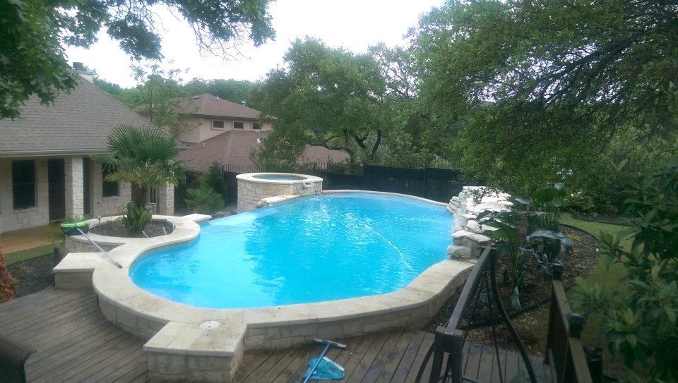 Backyard with a blue swimming pool, patio furniture, and trees beside a house