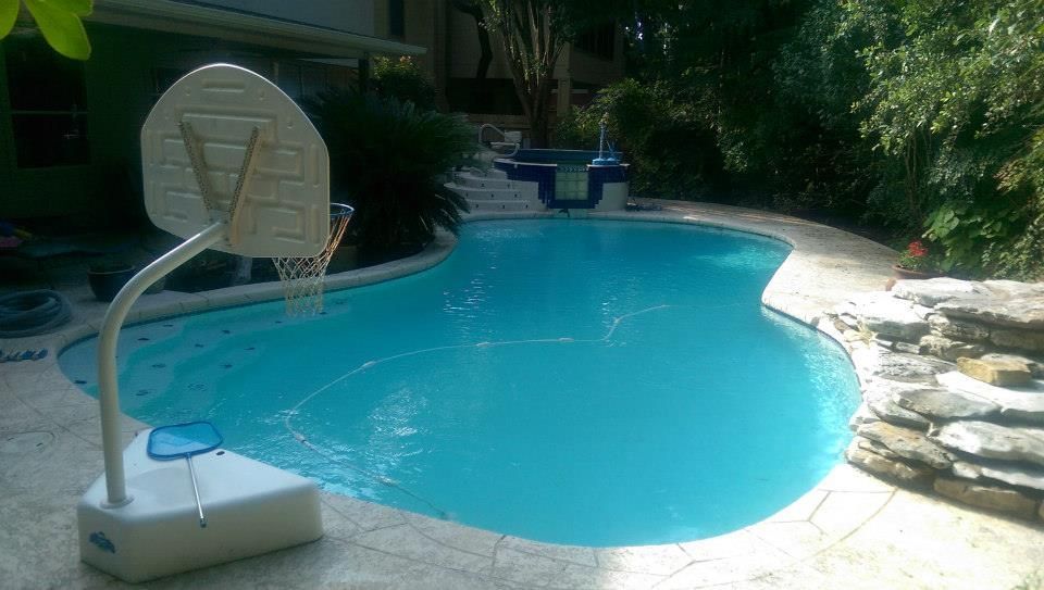 Backyard swimming pool with a basketball hoop and stone patio surrounded by trees