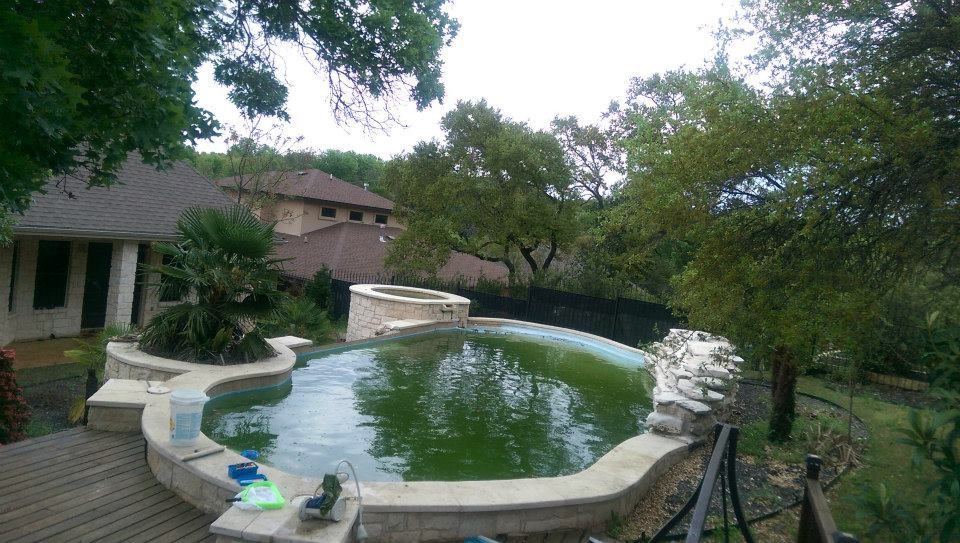 Backyard pool with stone edge and trees beside a rustic house