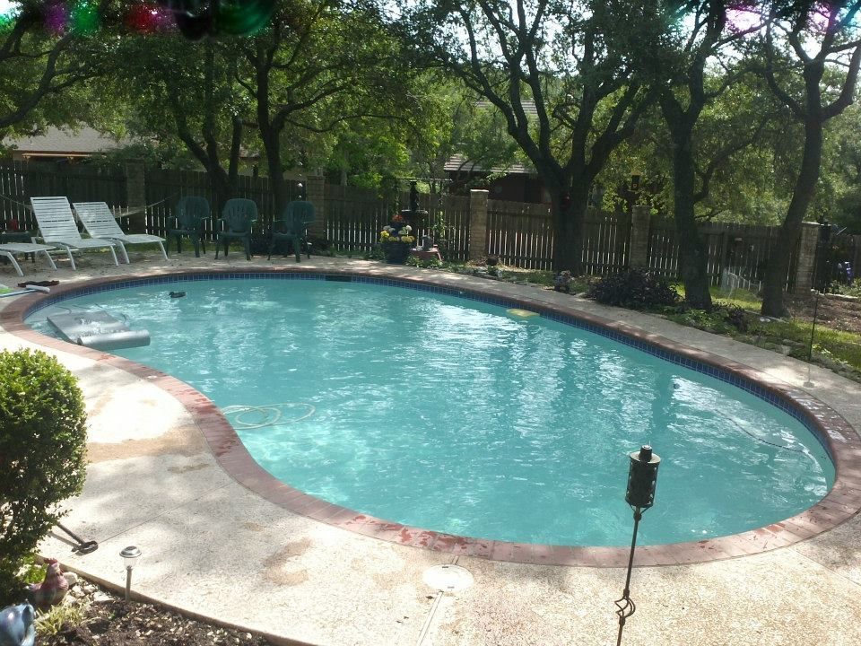 Curved outdoor swimming pool with blue water, surrounded by trees, lounge chairs, and a concrete deck.