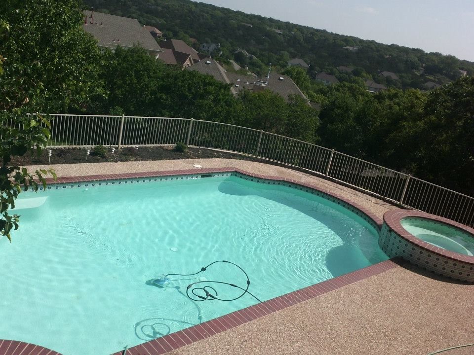 Backyard swimming pool with turquoise water, hot tub, and hillside view beyond a metal fence