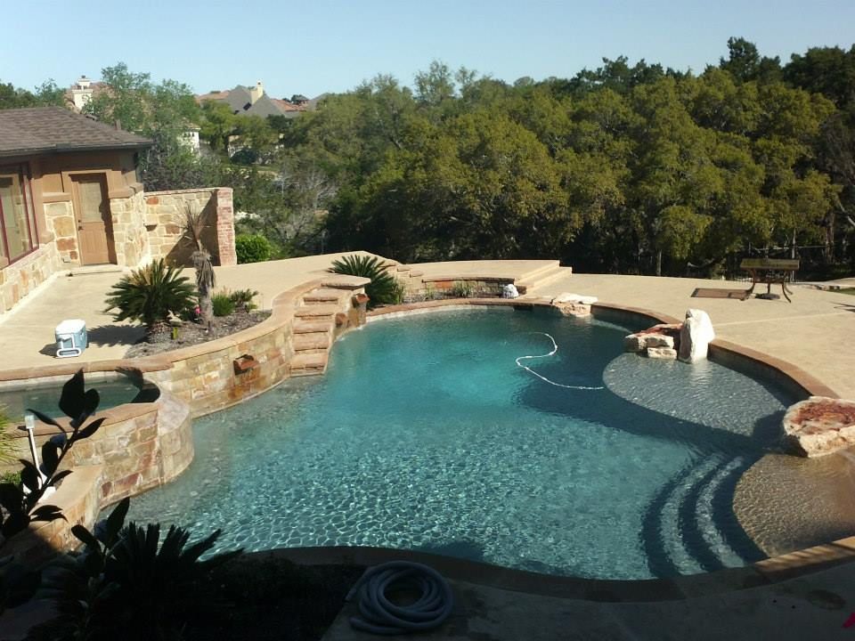 Backyard pool with turquoise water, stone patio, and surrounding trees in bright sunlight