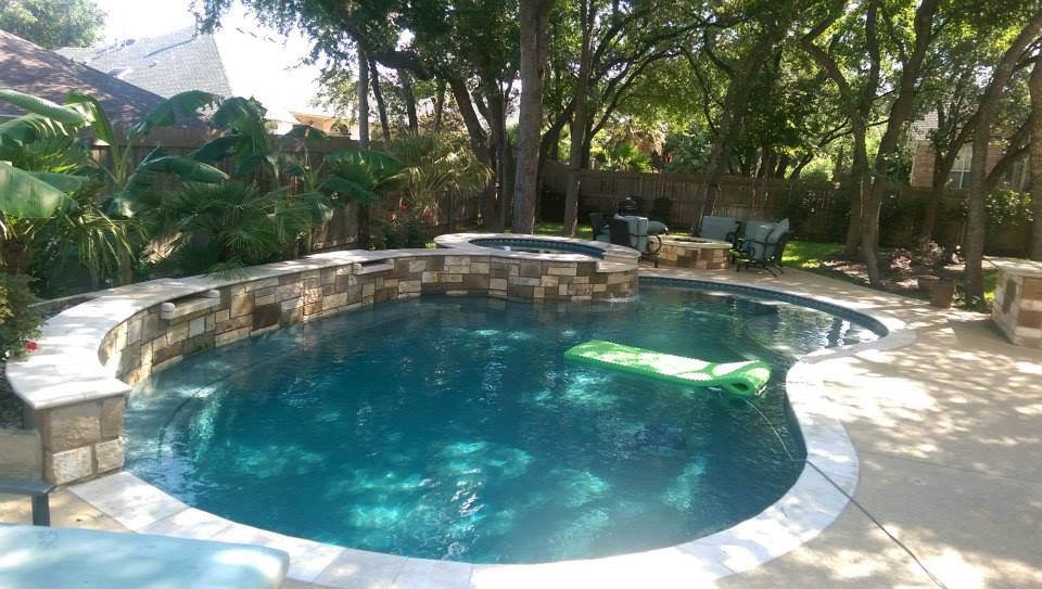 Round stone pool surrounded by trees and patio seating in a shaded garden courtyard