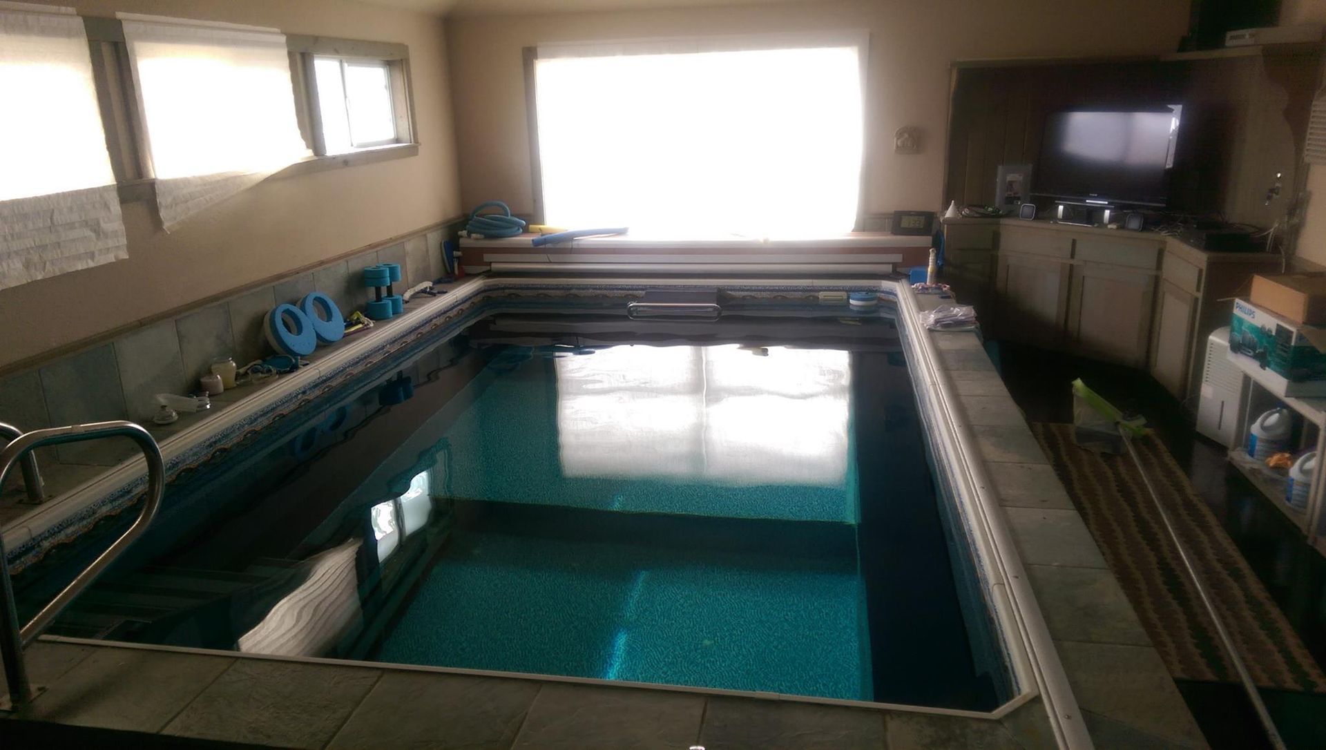 Indoor swimming pool with clear blue water, tiled deck, and windows letting in daylight.