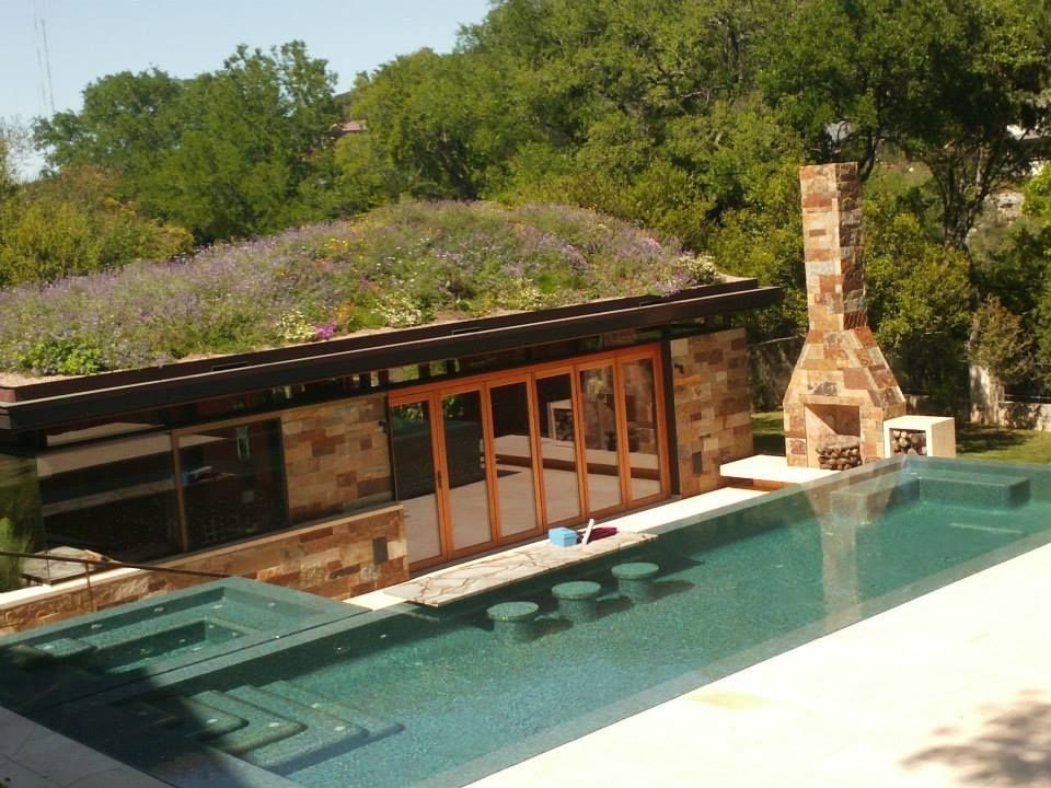 Modern pool beside a stone patio and low house, with trees and a hillside in the background