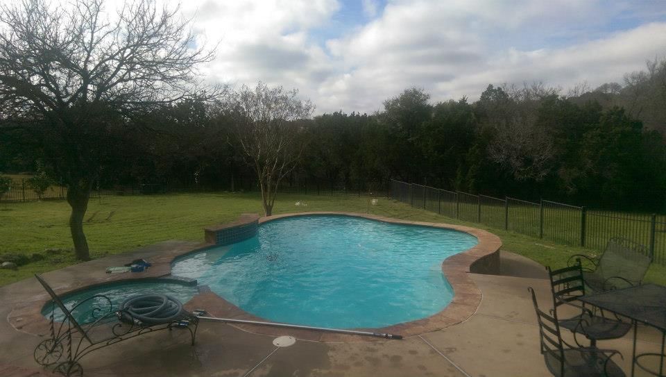 Backyard swimming pool with turquoise water, surrounded by patio chairs and trees.