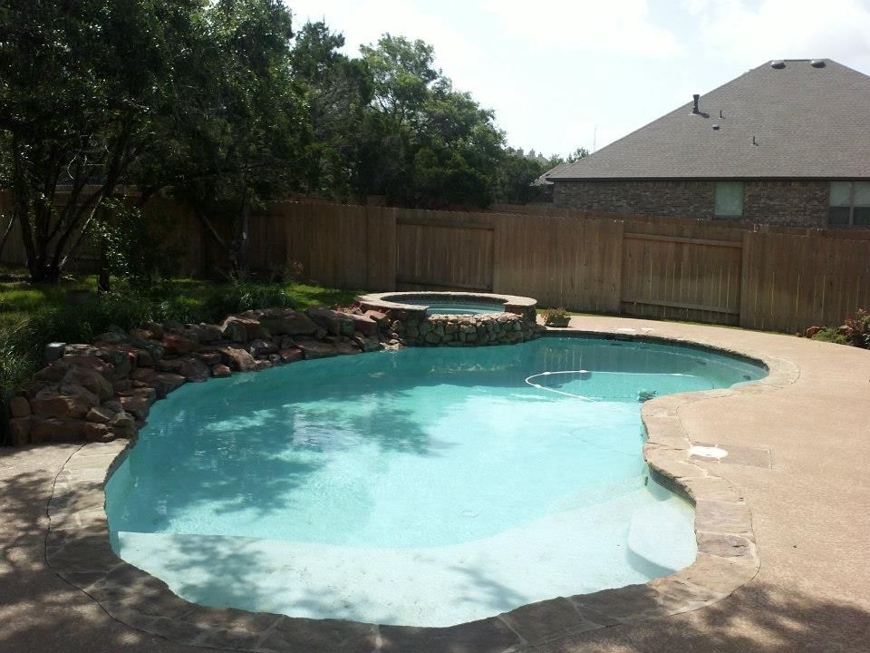 Backyard swimming pool with turquoise water, stone edging, and a wooden privacy fence