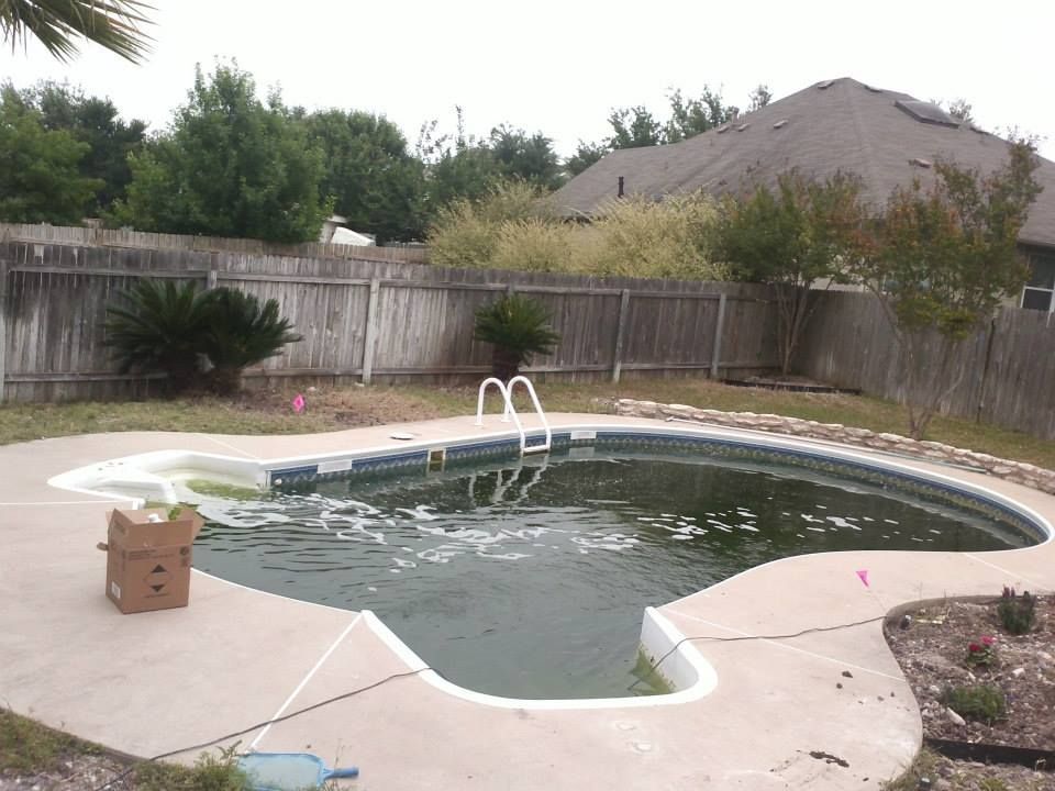 Backyard swimming pool with cloudy water, diving board, and wooden fence under overcast sky