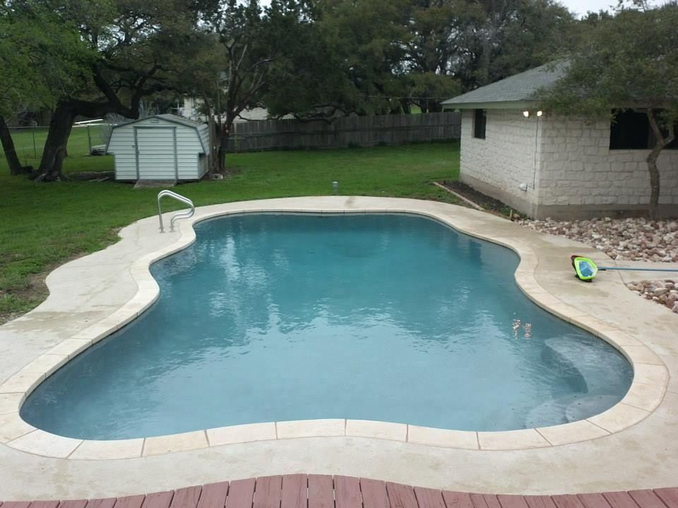 Backyard swimming pool with light blue water, white coping, and a house beside it