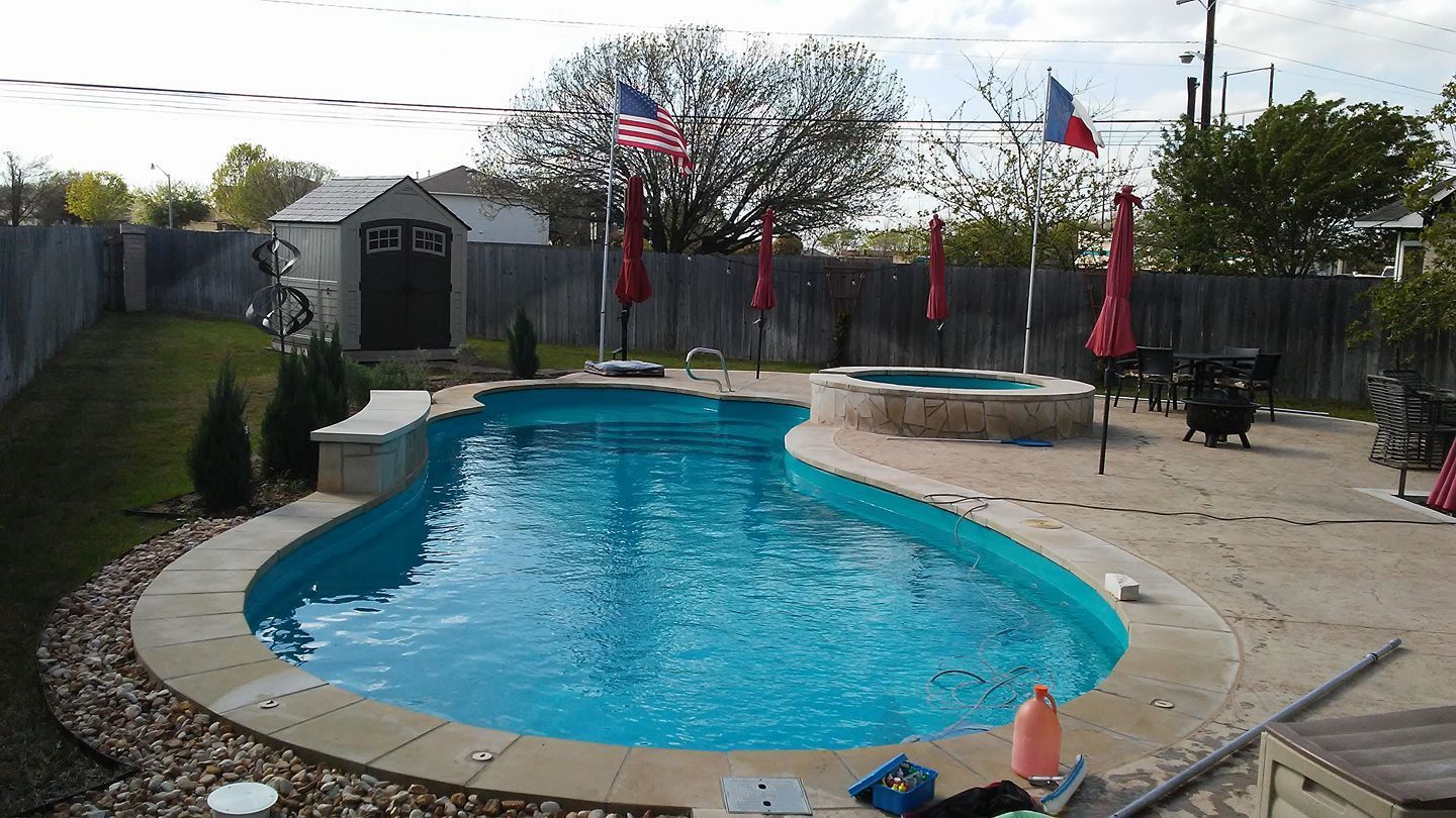 Backyard swimming pool with blue water, red umbrellas, and patio chairs on a sunny day